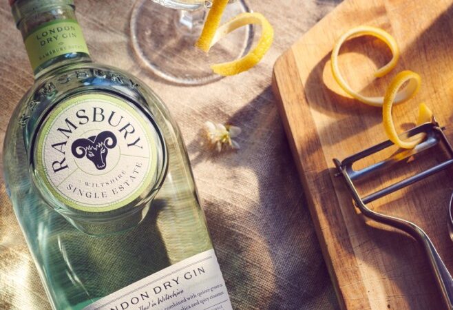 Ramsbury Single Estate London Dry Gin bottle alongside a coupe glass garnished with a lemon twist on a textured linen surface.