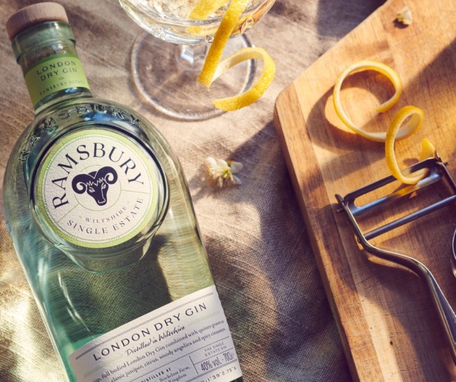 Ramsbury Single Estate London Dry Gin bottle alongside a coupe glass garnished with a lemon twist on a textured linen surface.